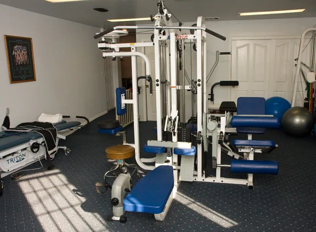 Home gym interior with white exercise machine, blue seating, stationary bike, and fitness equipment