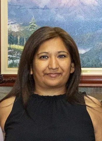 Woman with long dark hair smiling at camera, wearing black sleeveless top